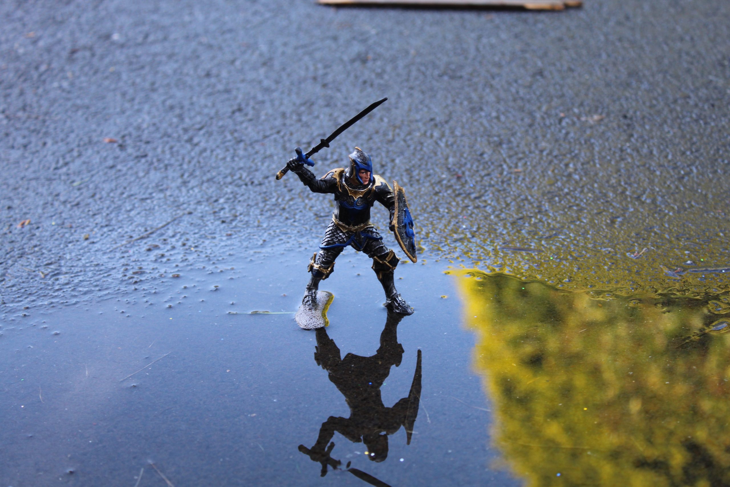 small model of armoured medieval person wielding a sword placed on a puddle outside.